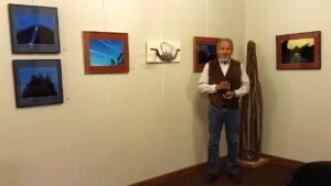 Durango Mendoza in vest and dress pants poses among his photographs at a gallery